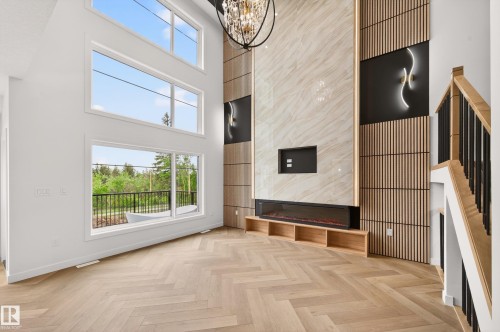 Two-story living area featuring a prominent fireplace wall with integrated shelving, large windows, wood-finish herringbone flooring, and a contemporary chandelier - 431 172 Avenue, Edmonton, AB - Indoor Photo Showing Other Room