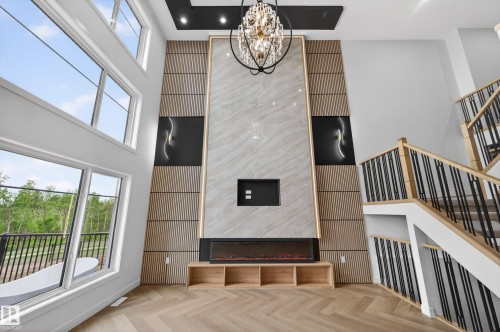 Double-height living space featuring an electric fireplace with a floor-to-ceiling stone-look surround, integrated shelving, and a decorative chandelier - 431 172 Avenue, Edmonton, AB - Indoor Photo Showing Other Room