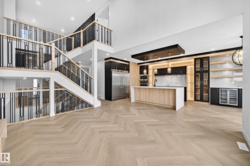 Open-concept living space featuring herringbone wood-finish flooring, a contemporary kitchen with a large island and integrated appliances, and a multi-level staircase with modern black and wood railings - 431 172 Avenue, Edmonton, AB - Indoor