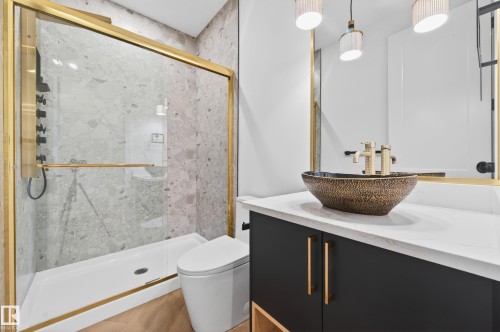 Contemporary bathroom featuring a glass-enclosed shower with gold-finish hardware, a textured vessel sink with gold-finish faucet, a dark vanity with gold-tone pulls, a floating mirror with gold-tone frame, and wood-finish flooring - 431 172 Avenue, Edmonton, AB - Indoor Photo Showing Bathroom