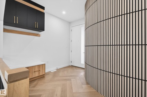 Entryway featuring a curved slatted wood wall, herringbone-patterned wood-finish flooring, built-in black cabinetry with gold hardware, a white built-in bench with wood-finish drawers, and a wood-finish stair railing - 431 172 Avenue, Edmonton, AB - Indoor Photo Showing Other Room