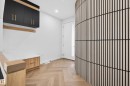 Entryway featuring a curved slatted wood wall, herringbone-patterned wood-finish flooring, built-in black cabinetry with gold hardware, a white built-in bench with wood-finish drawers, and a wood-finish stair railing - 431 172 Avenue, Edmonton, AB  - Indoor Photo Showing Other Room 