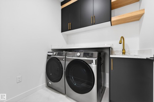 Laundry area featuring black cabinetry with gold hardware, a white countertop, a gold-finish faucet, and open wood-finish shelving - 431 172 Avenue, Edmonton, AB - Indoor Photo Showing Laundry Room