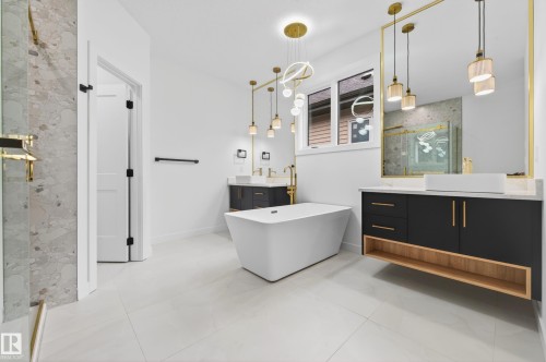 Spacious bathroom featuring a freestanding soaking tub, dual floating vanities with vessel sinks, a large mirror with gold-tone framing, and tiled flooring - 431 172 Avenue, Edmonton, AB - Indoor Photo Showing Bathroom