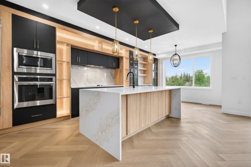 Kitchen featuring a large waterfall island with integrated sink and matte black faucet, herringbone wood-finish flooring, built-in stainless steel appliances, and a full-height window - 431 172 Avenue, Edmonton, AB - Indoor Photo Showing Kitchen