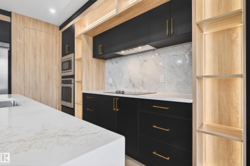Modern kitchen featuring dark cabinetry with gold hardware, integrated stainless steel appliances, a white quartz island with an undermount sink, a white marble backsplash, and wood-finish shelving with integrated lighting - 431 172 Avenue, Edmonton, AB - Indoor Photo Showing Kitchen With Upgraded Kitchen