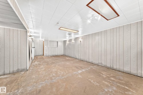 Spacious room featuring light-colored vertical paneling, a white paneled ceiling, and concrete flooring - 10819 137 Avenue Nw, Edmonton, AB - Indoor Photo Showing Other Room