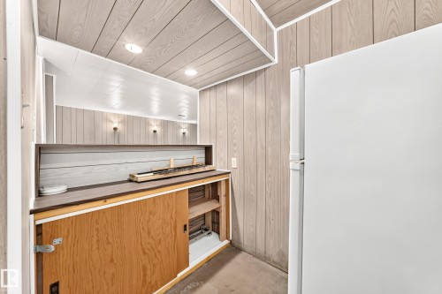 Utility area featuring light wood-finish vertical paneling, a built-in countertop with open shelving, and integrated lighting - 10819 137 Avenue Nw, Edmonton, AB - Indoor Photo Showing Other Room
