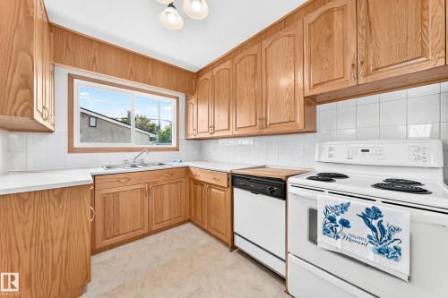Kitchen featuring wood cabinetry, white countertops, a white tile backsplash, a double basin sink, and a white electric range - 10819 137 Avenue Nw, Edmonton, AB - Indoor Photo Showing Kitchen With Double Sink