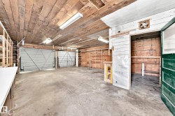 Spacious garage with concrete flooring, two roll-up garage doors, exposed wood-plank ceiling, and built-in shelving - 
