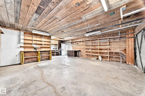 Spacious garage featuring a concrete floor, extensive built-in shelving, wood plank walls, a wood plank ceiling, and fluorescent lighting - 10819 137 Avenue Nw, Edmonton, AB - Indoor Photo Showing Garage