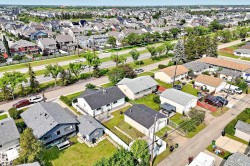 Aerial view showcasing a residential neighborhood with diverse housing styles, mature trees, and a multi-lane thoroughfare - 