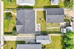 Aerial view showcasing a residential property with a dark shingle roof and a green lawn - 