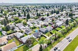 Aerial perspective of a residential neighborhood featuring detached single-story homes with pitched roofs, front yards, and mature trees - 
