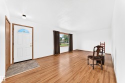 Entry area featuring a white front door with a decorative glass transom, wood-finish flooring, and a window with dark curtains - 