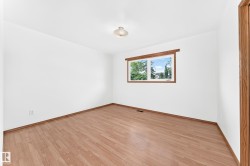 Bright room featuring wood-finish flooring, white walls, and a window with wood trim - 