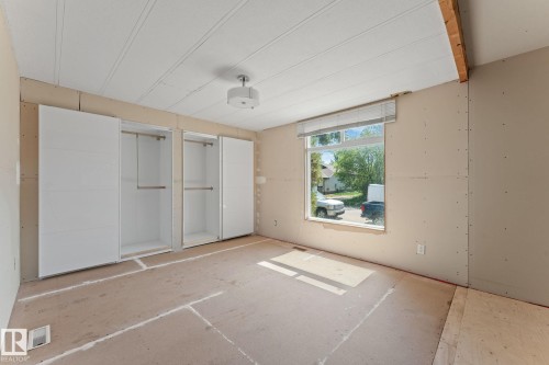 Interior room featuring a large window, two white built-in wardrobes with hanging rods, a ceiling-mounted light fixture, and an exposed ceiling beam - 219 Lee Ridge Road, Edmonton, AB - Indoor Photo Showing Other Room