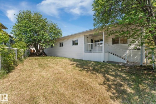 Rear exterior featuring white vinyl siding, a covered deck with white railing, and a fenced yard with mature trees - 219 Lee Ridge Road, Edmonton, AB - Outdoor