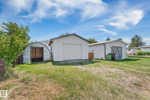 Exterior featuring a white detached garage with a roll-up door, a secondary white outbuilding with double wooden doors, and a rustic barn-style shed - 219 Lee Ridge Road, Edmonton, AB - Outdoor