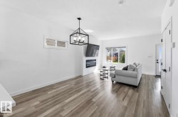 Spacious living area featuring wood-finish flooring, a contemporary fireplace with white tile surround, and a large window providing outdoor illumination - 