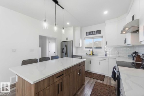 Contemporary kitchen featuring a large center island with a light-toned countertop, wood-finish cabinetry, and pendant lighting - 17924 61 Street Nw, Edmonton, AB - Indoor Photo Showing Kitchen With Upgraded Kitchen