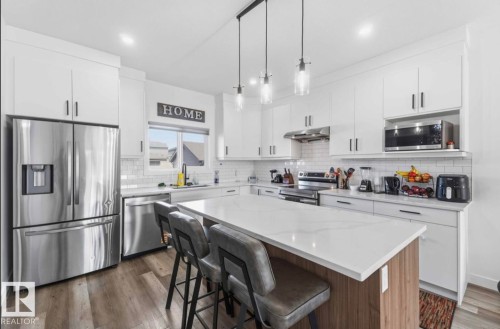 Modern kitchen featuring white cabinetry, stainless steel appliances, and a central island with a light-toned countertop - 17924 61 Street Nw, Edmonton, AB - Indoor Photo Showing Kitchen With Stainless Steel Kitchen With Upgraded Kitchen