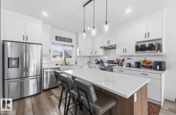 Modern kitchen featuring white cabinetry, stainless steel appliances, and a central island with a light-toned countertop - 