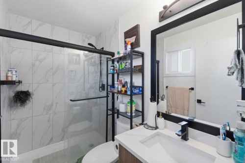 Bathroom featuring a glass-enclosed shower with white marble-look tile, a single vanity with a white rectangular sink, a black framed mirror, and matte black fixtures - 17924 61 Street Nw, Edmonton, AB - Indoor Photo Showing Bathroom