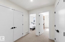 Hallway featuring light-toned carpeting, white walls, and modern white doors with black hardware - 
