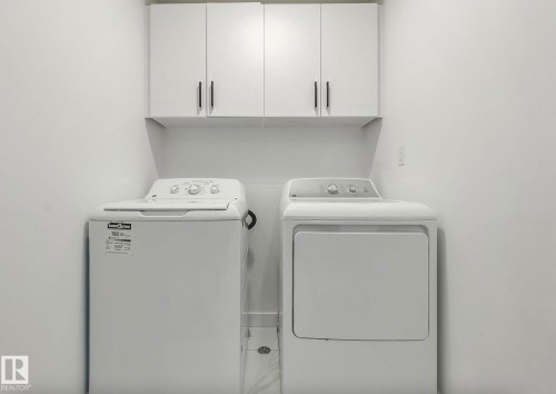 Dedicated laundry area featuring white wall-mounted cabinetry with dark pulls, a white top-load washing machine, and a white front-load dryer - 17924 61 Street Nw, Edmonton, AB - Indoor Photo Showing Laundry Room