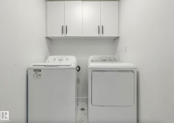 Dedicated laundry area featuring white wall-mounted cabinetry with dark pulls, a white top-load washing machine, and a white front-load dryer - 