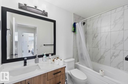 Bathroom featuring a wood-finish vanity with a white countertop and integrated sink, a large framed mirror, a three-light vanity fixture, and a tiled tub shower combination - 17924 61 Street Nw, Edmonton, AB - Indoor Photo Showing Bathroom