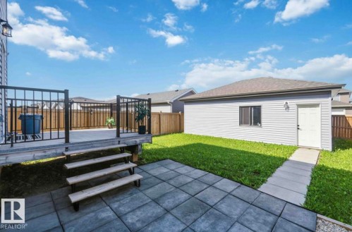 Backyard featuring an elevated wood deck with black metal railings, a ground-level paver patio, a detached exterior structure with vinyl siding and a shingled roof, a grass lawn, and a privacy fence - 17924 61 Street Nw, Edmonton, AB - Outdoor