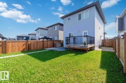 Expansive backyard featuring a vibrant green lawn, a wooden privacy fence, a raised wooden deck with black railings, and a gravel side yard - 