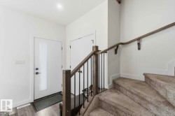 Entryway featuring a contemporary white door with frosted glass panel, matte black hardware, and wood-finish flooring - 