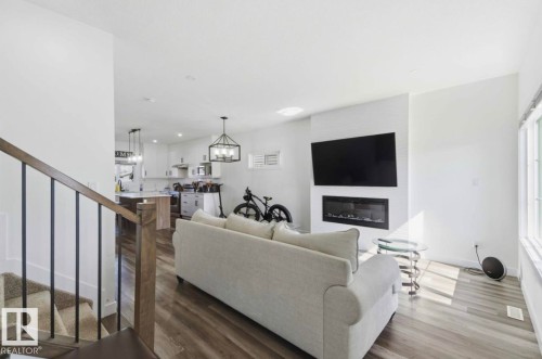 Living area featuring wood-finish flooring, a contemporary fireplace with a white tile surround, and a large window - 17924 61 Street Nw, Edmonton, AB - Indoor Photo Showing Living Room With Fireplace