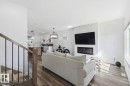 Living area featuring wood-finish flooring, a contemporary fireplace with a white tile surround, and a large window - 17924 61 Street Nw, Edmonton, AB  - Indoor Photo Showing Living Room With Fireplace 