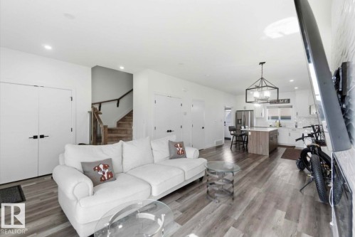 Open-concept living area featuring light wood-finish flooring, recessed lighting, a contemporary kitchen with white cabinetry and a center island, and a geometric pendant light fixture - 17924 61 Street Nw, Edmonton, AB - Indoor Photo Showing Living Room