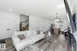 Open-concept living area featuring light wood-finish flooring, recessed lighting, a contemporary kitchen with white cabinetry and a center island, and a geometric pendant light fixture - 
