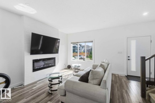 Living area featuring a textured accent wall with a built-in electric fireplace, wood-finish flooring, and a contemporary entry door with a frosted glass insert - 17924 61 Street Nw, Edmonton, AB - Indoor Photo Showing Living Room With Fireplace