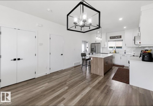 Open-concept kitchen featuring wood-finish flooring, a central island with a light countertop, white cabinetry with dark hardware, and a white subway tile backsplash - 17924 61 Street Nw, Edmonton, AB - Indoor Photo Showing Kitchen