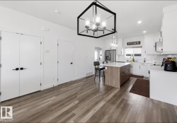 Open-concept kitchen featuring wood-finish flooring, a central island with a light countertop, white cabinetry with dark hardware, and a white subway tile backsplash - 