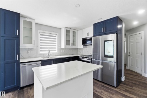Kitchen featuring two-tone cabinetry with glass-front uppers, stainless steel appliances, a center island with a solid surface countertop, and wood-finish flooring - #64 120 Magrath Rd Nw, Edmonton, AB - Indoor Photo Showing Kitchen With Upgraded Kitchen