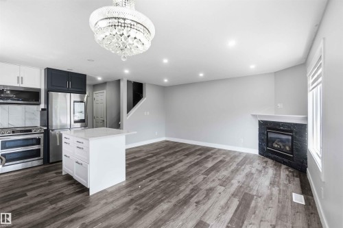Open-concept living space with wood-finish flooring, a contemporary fireplace with a dark stone surround, and recessed lighting - #64 120 Magrath Rd Nw, Edmonton, AB - Indoor Photo Showing Kitchen With Fireplace