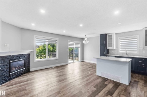 Open-concept living space with wood-finish flooring, a contemporary fireplace featuring black stacked stone, and recessed lighting - #64 120 Magrath Rd Nw, Edmonton, AB - Indoor With Fireplace