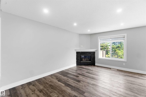 Living space featuring a stone-faced fireplace with a white mantel, wood-finish flooring, and recessed ceiling lighting - #64 120 Magrath Rd Nw, Edmonton, AB - Indoor Photo Showing Living Room With Fireplace
