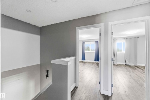 Upper-level hallway with recessed lighting and a balustrade, featuring two rooms with wood-finish flooring and windows with natural light - #64 120 Magrath Rd Nw, Edmonton, AB - Indoor Photo Showing Other Room