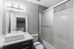 Modern bathroom featuring a white vessel sink on a light-colored countertop, a dark wood-finish vanity with drawer pulls, and a bathtub with sliding frosted glass doors - 