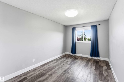 Room featuring wood-finish flooring, light gray walls, white baseboards, and a window with blue drapes and a black rod - #64 120 Magrath Rd Nw, Edmonton, AB - Indoor Photo Showing Other Room