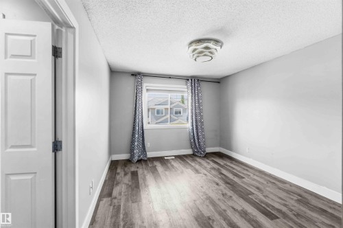 Room featuring wood-finish flooring, a window with a dark curtain rod, a semi-flush mount ceiling light fixture, a paneled interior door, and white baseboards - #64 120 Magrath Rd Nw, Edmonton, AB - Indoor Photo Showing Other Room